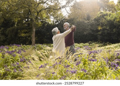 Happy senior biracial couple dancing with flowers around them in garden at home. Senior lifestyle, retirement, nature and domestic life, unaltered. - Powered by Shutterstock