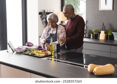 Happy senior biracial couple preparing vegetables and embracing in kitchen at home. Senior lifestyle, retirement, food, cooking and domestic life, unaltered. - Powered by Shutterstock