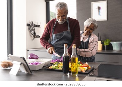 Happy senior biracial couple wearing aprons preparing vegetables in kitchen at home. Senior lifestyle, retirement, food, cooking and domestic life, unaltered. - Powered by Shutterstock