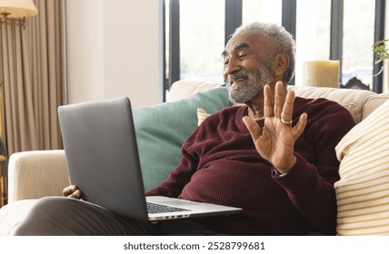 Happy senior biracial man sitting on couch and having laptop video call at home. Senior lifestyle, retirement, communication and domestic life, unaltered. - Powered by Shutterstock