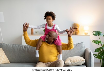 Happy Senior Black Man Play With Small Girl, Grandfather Carrying Granddaughter On His Shoulders, Enjoying Free Time, Have Fun In Living Room Interior. Vacation, Family, Relationships And Game At Home