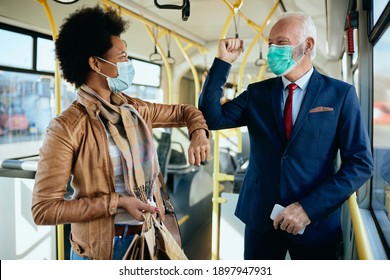 Happy Senior Businessman And His Black Female Friend Greeting With Elbows In A Public Transport During Coronavirus Pandemic. 