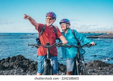 Happy senior caucasian couple wearing helmets riding on the beach with electric bicycles. Authentic elderly retired life concept. Horizon over sea - Powered by Shutterstock