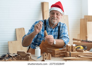 Happy senior caucasian man wearing Santa hat holding and looking at his small wooden Christmas tree, prepare toys ready for Christmas - Powered by Shutterstock