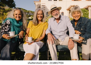 Happy senior citizens smiling at the camera while relaxing outside a retirement home. Group of carefree elderly people having tea together and enjoying their golden years.