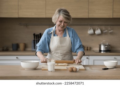 Happy senior cook blogger woman baking in home kitchen, rolling dough on floury board, preparing bakery food dessert, smiling, laughing, shooting culinary workshop - Powered by Shutterstock