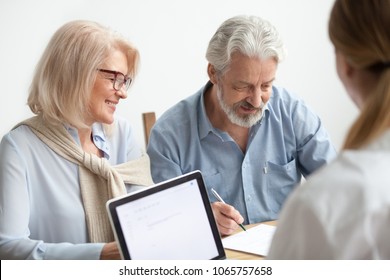 Happy senior couple about to sign document at meeting with financial advisor, older man agrees to put signature on contract making investment purchase, taking insurance, aged family in travel office