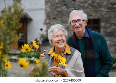 Happy Senior Couple At Autumn City Walk, Posing With Flowers.