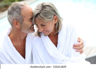 Happy Senior Couple In Bathrobe By Resort Pool