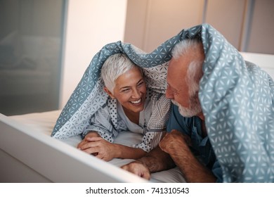 A Happy Senior Couple Being Silly In Bed On A Beautiful Sunny Morning.