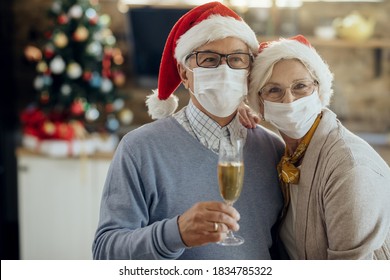 Happy Senior Couple Celebrating Christmas At Home And Wearing Protective Face Masks Due To Coronavirus Pandemic. 