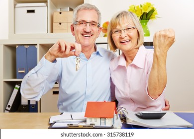 Happy Senior Couple Cheering Together With Small House And Door Keys