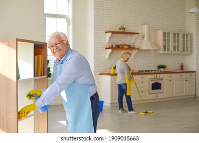 Happy senior couple cleaning their house. Mature husband helping his wife to tidy up at home. Smiling elderly man dusting the shelves while the woman is mopping the floor in their new apartment