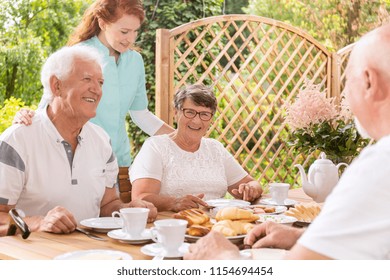 Happy Senior Couple Eating Breakfast And A Nurse Taking Care Of Them In The Garden