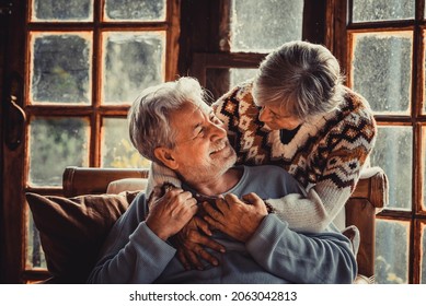 Happy Senior Couple Enjoy With Love Winter Holidays At Home Hugging With Joy And Romance. Romantic Elderly Lifestyle. Man And Woman Embrace And Look Each Other At Home With Snow Outside