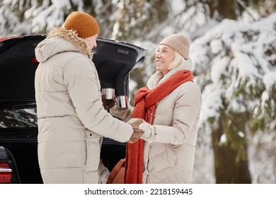 Happy Senior Couple Enjoying Cup Of Hot Coco Outdoors In Winter Forest And Holding Hands