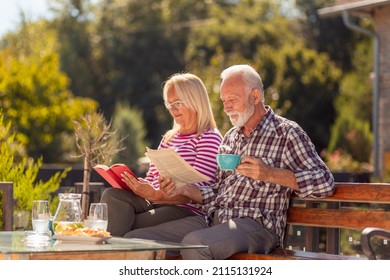 Happy senior couple enjoying their time together having an outdoor breakfast in the backyard of their home, man reading newspaper while woman is reading a book - Powered by Shutterstock