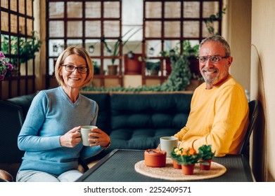 Happy senior couple enjoying their time together while drinking coffee outdoor in the backyard or on a terrace or balcony of their home. Both looking at the camera. Copy space. - Powered by Shutterstock