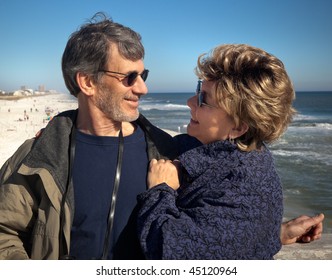 Happy senior couple enjoying themselves at a beautiful beach on their winter or spring vacation. Closeup view of the couple gazing at each other with the beach and ocean in the background. - Powered by Shutterstock