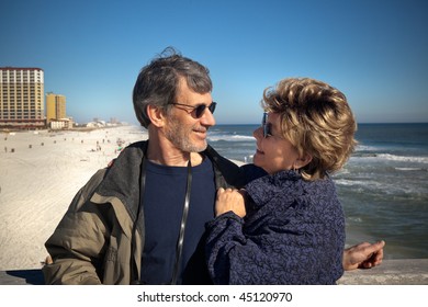 Happy senior couple enjoying themselves at a beautiful beach on their winter or spring vacation. Wide view of Couple gazing at each other with the beach, ocean and hotels in the background. - Powered by Shutterstock