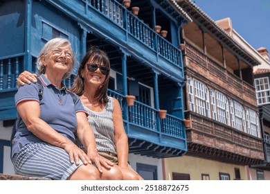 Happy senior couple of females friends sitting outdoors enjoying a sunny day on a leisure trip. Typical canary island balconies in the background - Powered by Shutterstock