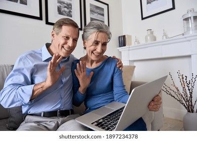 Happy Senior Couple Greeting Family Making Online Video Call On Laptop. Middle Aged Old Grandparents Waving Hands Enjoying Virtual Distance Meeting Zoom Chat Looking At Computer Sit On Couch At Home.