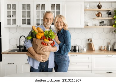 Happy Senior Couple With Grocery Bag In Hands Standing In Kitchen Interior, Smiling Mature Spouses Holding Organic Vegetables, Posing After Groceries Shopping, Advertising Supermarket Food Delivery - Powered by Shutterstock