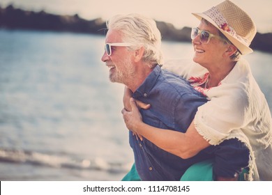 happy senior couple have fun and enjoy outdoor leisure activity at the beach. the man carry the woman on his back to enjoy together a retired lifestyle at the beach. smiling and laughing persons
