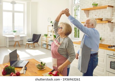 Happy Senior Couple Having Fun While Cooking Healthy Vegetarian Meal In The Kitchen Of Their Studio Apartment. Senior Citizens Leading Active Lifestyle, Enjoying Life, Spending Time Together At Home