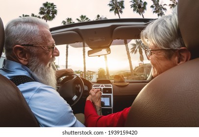 Happy senior couple having fun driving on new convertible car - Mature people enjoying time together during road trip tour vacation - Elderly lifestyle and travel culture transportation concept