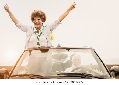 Happy Senior Couple Having Fun In Summer Vacation With Cabriolet Car At Sunset - Elderly Multiracial People Inside Convertible Car