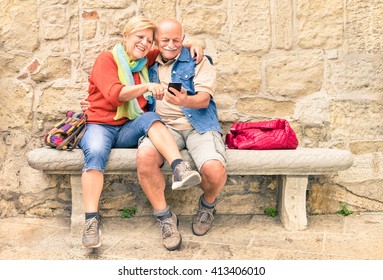 Happy Senior Couple Having Fun Together With Mobile Smart Phone - Concept Of Active Playful Elderly During Retirement - Travel Lifestyle Concept With Retired People - Warm Cloudy Afternoon Color Tones