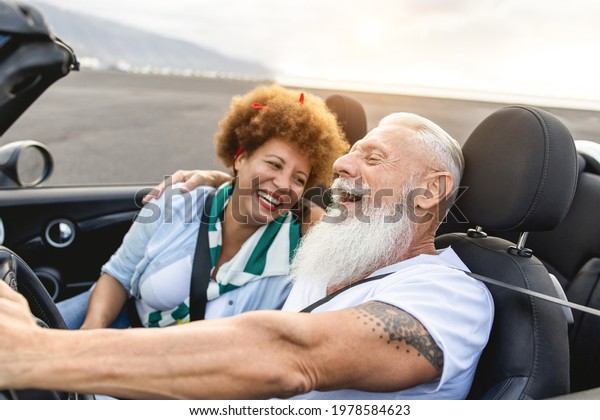 Happy senior couple having\
fun in convertible car during summer vacation - Focus on hipster\
man face