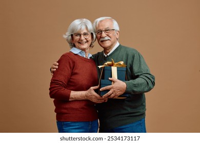 Happy senior couple holding black colored gift boxes with golden ribbon while looking at camera. Copy space. - Powered by Shutterstock