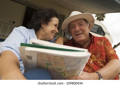 Happy Senior Couple Holding Map Book With Caravan In The Background