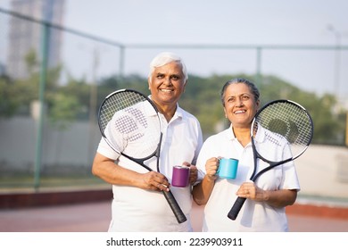 Happy senior couple holding tennis bats and coffee cup in court. - Powered by Shutterstock