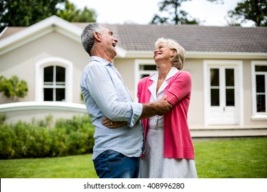 Happy Senior Couple Hugging Outside House In Yard