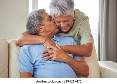 Happy Senior Couple Kiss, Hug And Smile With Love While Relax On The Sofa In The Living Room At Home. Playful, Fun Man And Woman Laughing, Smiling And Enjoying Retirement Life Together In Their