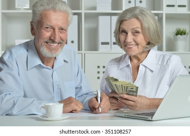 Happy Senior Couple With Laptop And Money In Office