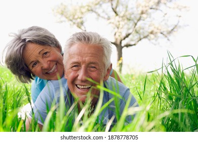 Happy Senior Couple Laying On The Grass In The Field On A Beautiful Spring Day.