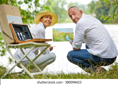 Happy senior couple learning painting in nature in summer on a lake - Powered by Shutterstock