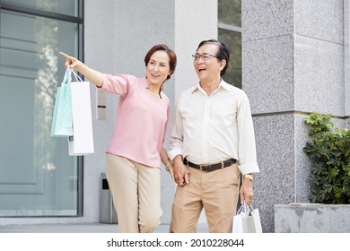 Happy Senior Couple Leaving Store With Manay Paper Bags In Hands After Shopping On Sale