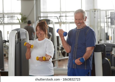 Happy senior couple lifting dumbbells at gym. Strength and power training for older adults.