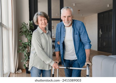 Happy senior couple looking at camera. Disabled incapacitated handicapped old elderly husband using walker walking frame for moving while wife helping him - Powered by Shutterstock