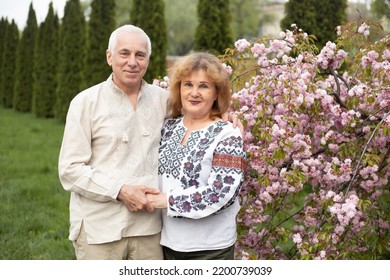 Happy Senior Couple In Love Having Fun In Summer Or Spring Nature Near Sakura Blooming Tree Wearing Ukrainian Embroidered Shirts