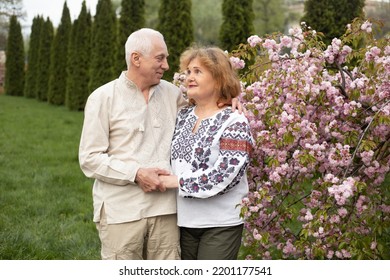 Happy Senior Couple In Love Having Fun In Summer Or Spring Nature Near Sakura Blooming Tree Wearing Ukrainian Embroidered Shirt