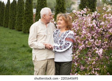 Happy Senior Couple In Love Having Fun In Summer Or Spring Nature Near Sakura Blooming Tree Wearing Ukrainian Embroidered Shirts