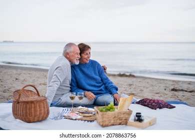 Happy senior couple in love sitting on blanket and having picnic outdoors on beach by sea. - Powered by Shutterstock