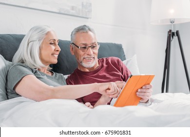 happy senior couple lying in bed and using tablet together - Powered by Shutterstock