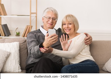 Happy Senior Couple Making Video Call On Phone And Waving To Caller